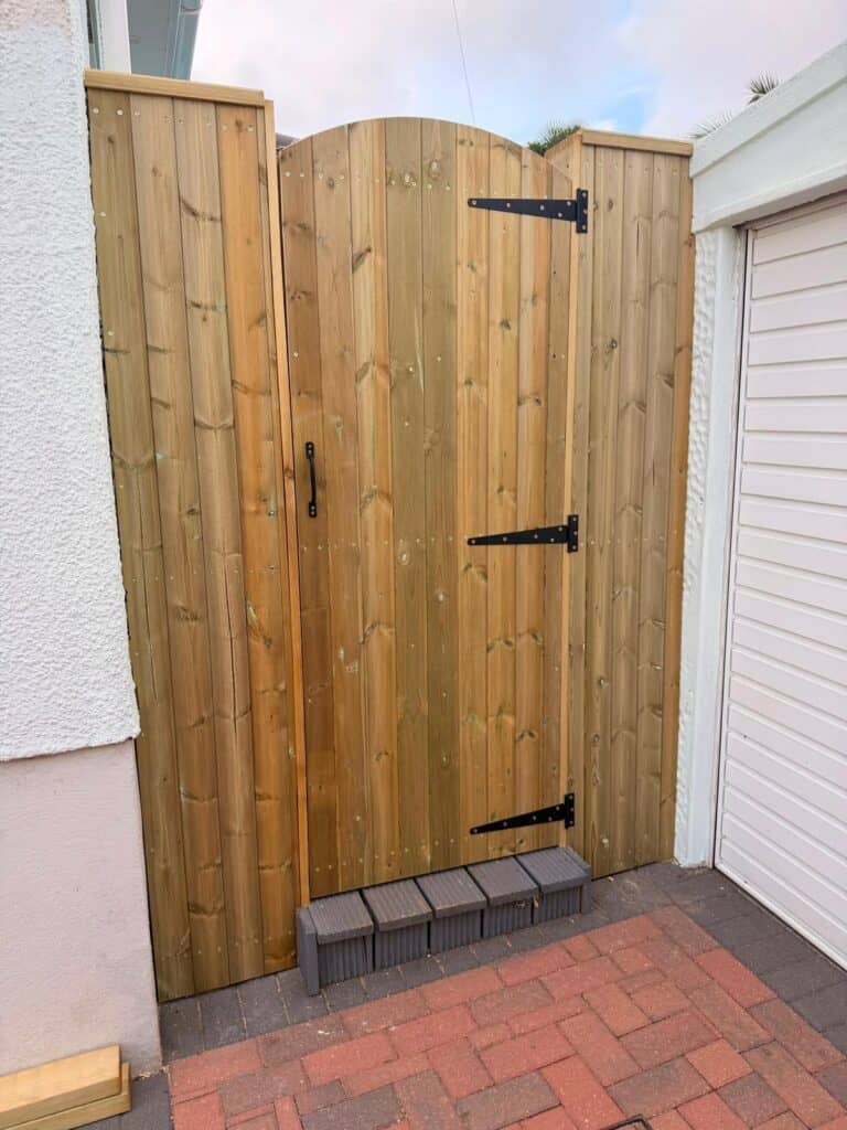 New wooden garden gate with black hinges and handle in a backyard.