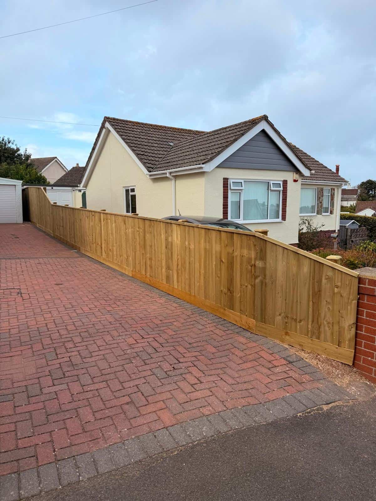 New wooden fence installed along driveway of modern house in UK.